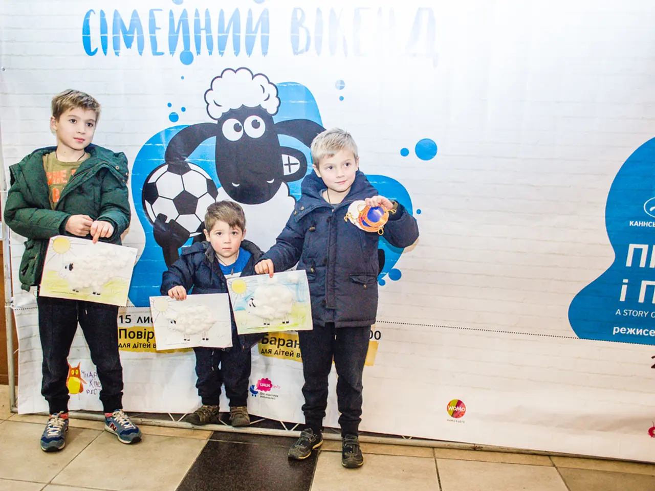In the middle of the image three children are standing and holding some papers. Behind them there...