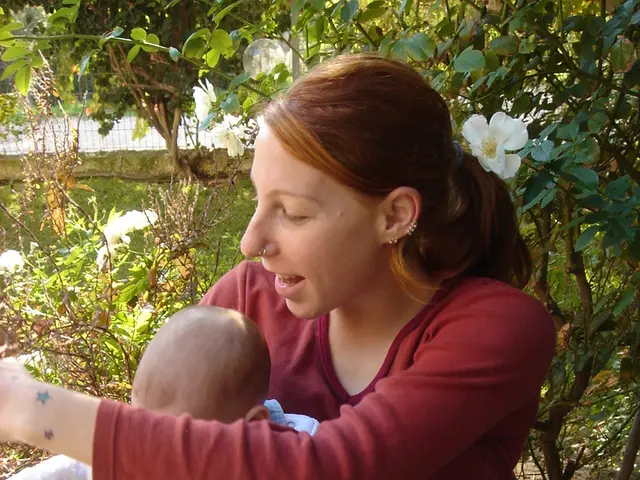 In this picture we can see a woman holding a baby and sitting on the chair. Some grass is visible...
