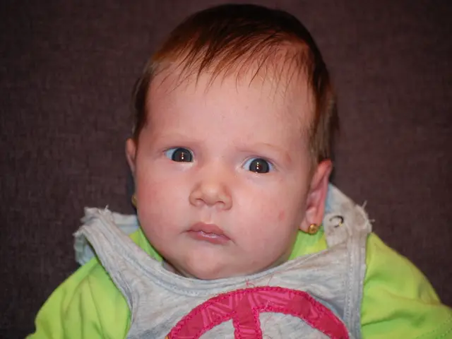 In this image there is a toddler sitting on the couch, behind the toddler there is a couch.