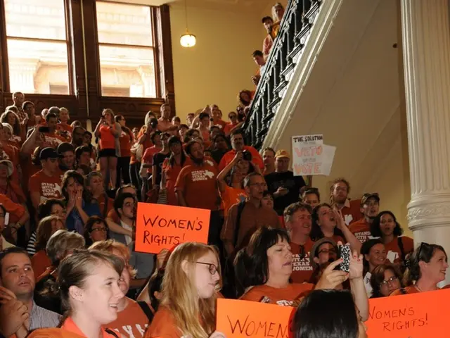 There are many people. Some are holding placard. Lady in the left is holding a mobile. Lady in the...